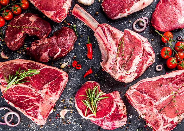 Various raw cuts of red meat, including steaks and a tomahawk chop, are arranged on a dark surface with herbs and spices—just like what you’d get from Karnivore Krate Premium Meat Subscription Boxes delivered nationwide.